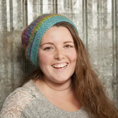 A woman with long hair and wearing a knit cap smiles 