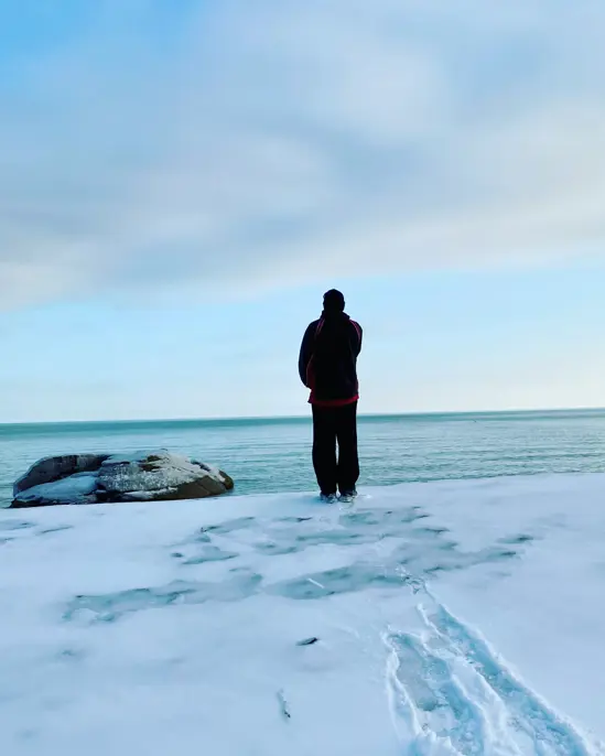 A person stands at the snow covered banks next to a large lake