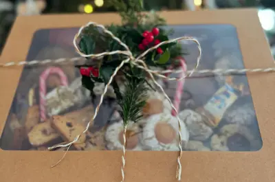 An arm holding a box of holidays cookies with a sprig of greenery tied on top