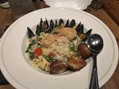 A plate of mixed seafood over creamy linguini sits on a white plate