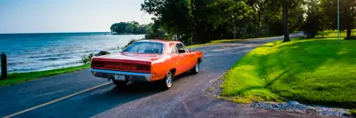 A red muscle car drives a country road at the edge of Lake Erie