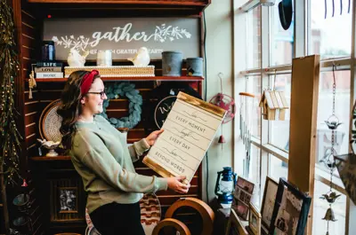 A woman holds a home decor sign surrounded by other gift items