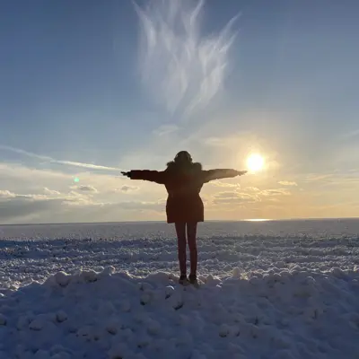 A woman stands with arms outstretched in front of a frozen lake