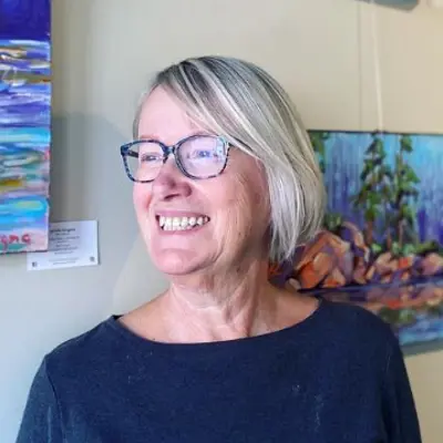 A woman stands in front of landscape artwork