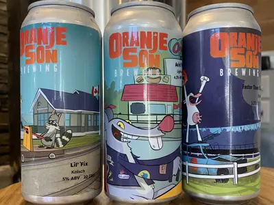 three cans of beer with colourful animal graphics on them sit atop wooden counter in front of a brewing pot