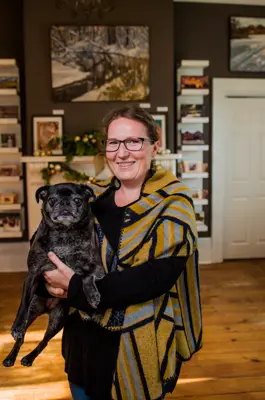 A woman holds a dog in front of her artwork