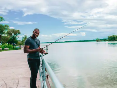 A man holds a fishing pole in a riverfront park