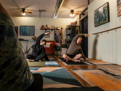 A couple seated on the floor stretch with one arm over their heads