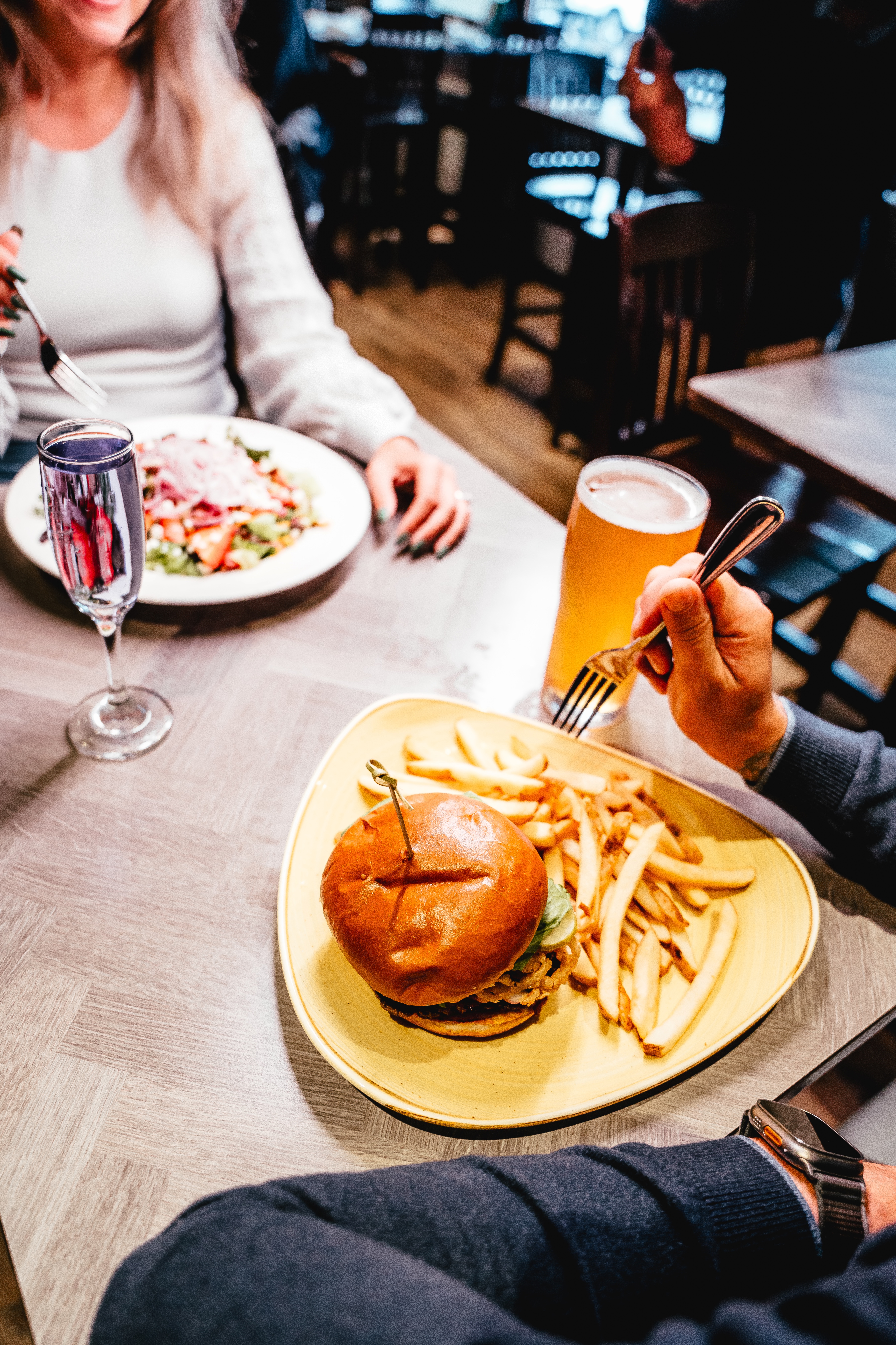 An overhead view of a restaurant table with burger and fries and large salad being enjoyed by a couple