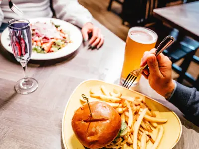 An overhead view of a restaurant table with burger and fries and large salad being enjoyed by a couple