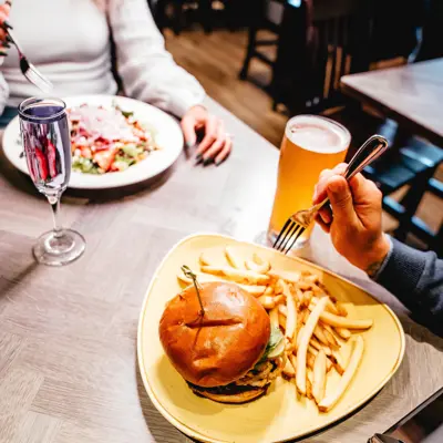 An overhead view of a restaurant table with burger and fries and large salad being enjoyed by a couple